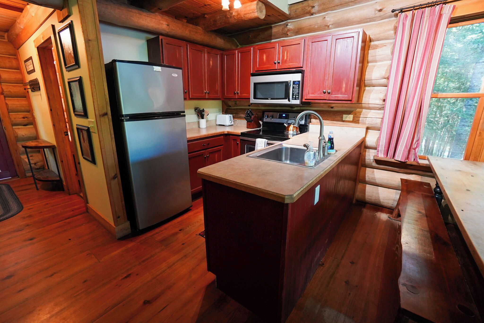 A log cabin kitchen with a refrigerator, microwave, sink, and wooden cabinets.