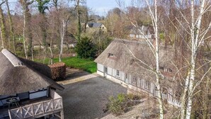 Un edificio tradicional con techo de paja, chimenea de piedra y terraza de madera.