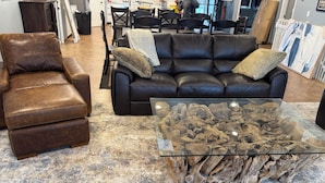 Un soggiorno con un divano in pelle marrone, un tavolino da caffè in vetro con decorazioni in legno e un tappeto decorato.