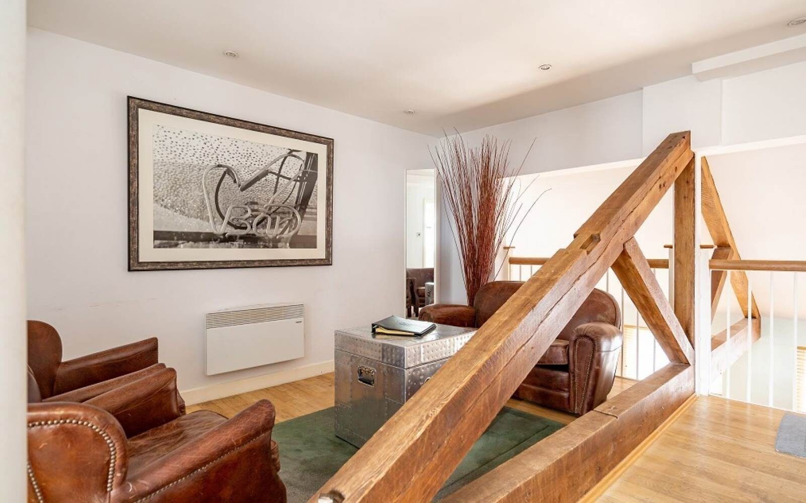 Un salon avec un escalier en bois, une œuvre d’art abstraite encadrée, des meubles en cuir et un radiateur.