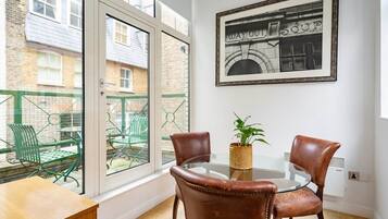 Ein Zimmer mit Glastisch, zwei Ledersesseln, einem Blumentopf und einem gerahmten Bild an der Wand.