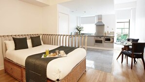 Habitación de hotel con cama, bandeja de desayuno, kitchenette, zona de comedor y vistas al exterior.