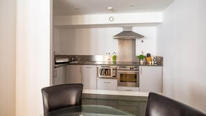 Een moderne keuken met roestvrijstalen apparatuur, een eethoek met een glazen tafel en een hoge plafond met inbouwverlichting.