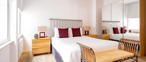 A modern hotel room with a large bed, bedside tables, a chair, a mirror, and a wardrobe.