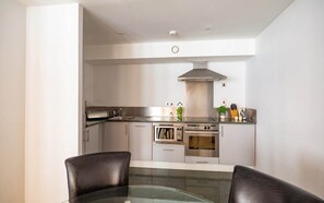 Une cuisine moderne dotée d’appareils électroménagers en acier inoxydable, un coin repas avec une table en verre et un plafond haut avec des luminaires encastrés.