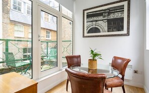 A room with a glass table, two leather chairs, a potted plant, and a framed picture on the wall. - 2 Bedroom Apartment in Liverpool Street (London)