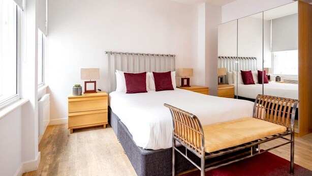 Een moderne hotelkamer met een groot bed, nachtkastjes, een stoel, een spiegel en een kledingkast.
