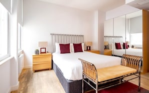 Ein modernes Hotelzimmer mit einem großen Bett, Nachttischen, einem Sessel, einem Spiegel und einem Kleiderschrank.