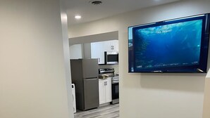 Een moderne keuken met witte kasten, een roestvrijstalen koelkast en een flatscreen televisie aan de muur.