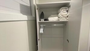 Een compacte kamer met een inbouwkast, een klein strijkplank en keurig opgevouwen handdoeken.
