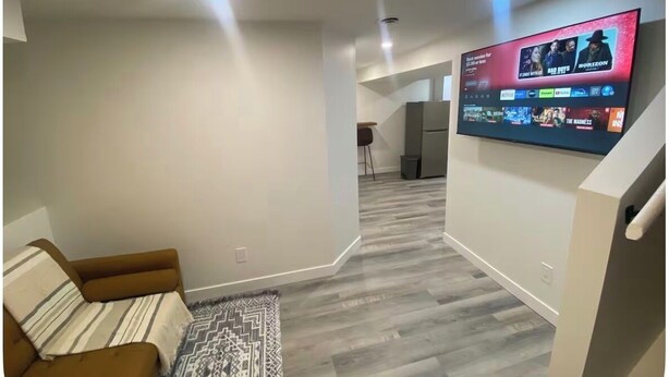 Een moderne woonkamer met een flatscreen televisie aan de muur, een bruine bank en een kamerbreed tapijt met een patroon.