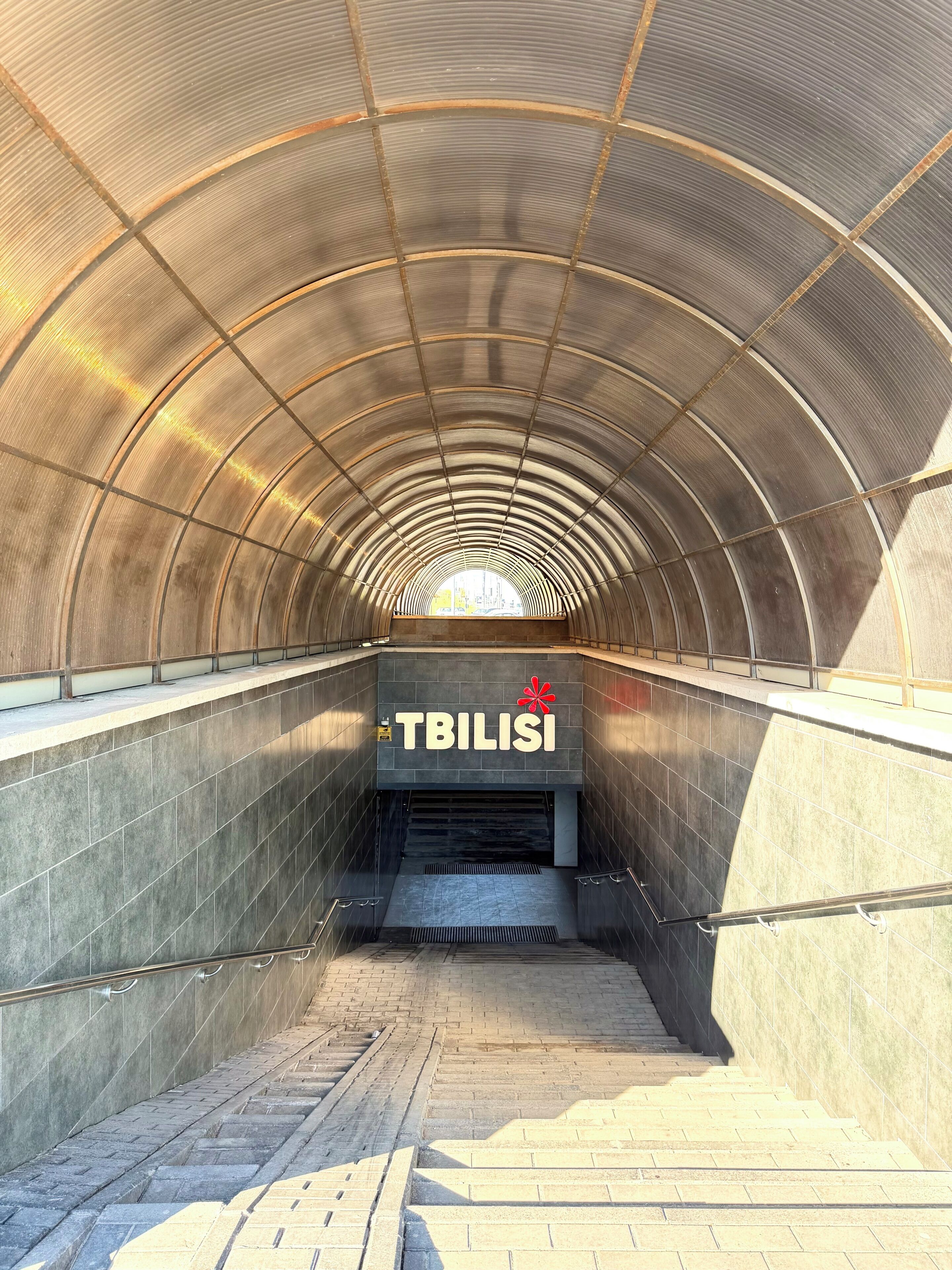 Eine tunnelartige Struktur mit einem Schild, auf dem 'TBILISI' steht, und einem roten Blumensymbol.