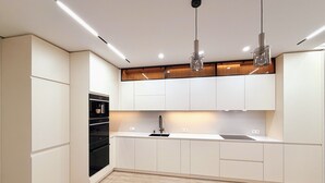Une cuisine moderne avec des meubles blancs, un four noir, un évier en acier inoxydable et deux luminaires suspendus.