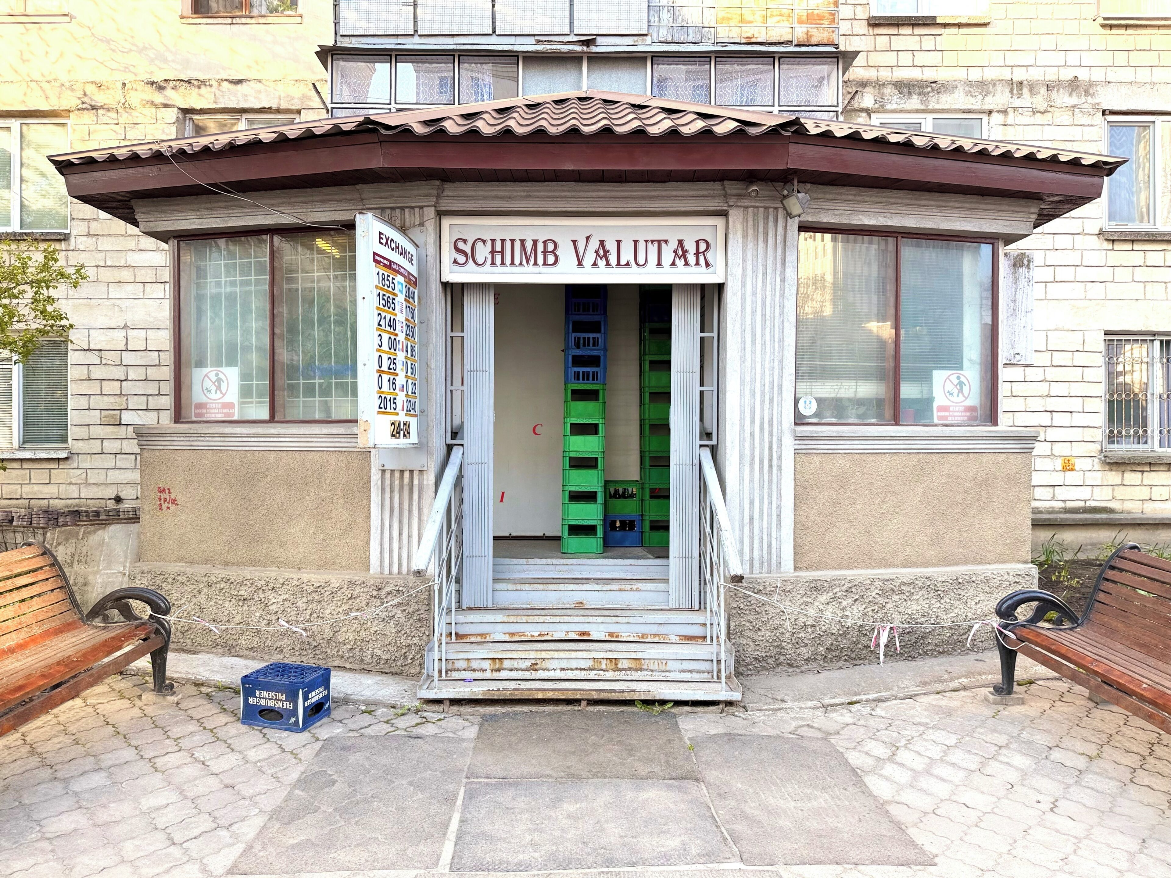 A building with a sign reading 'SCHIMB VALUTAR' and a staircase leading to a green interior.
