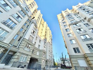 Un edificio residencial alto con varios balcones, entrada protegida por portón y cielo despejado.