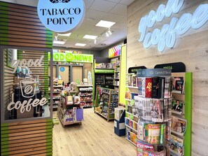 Una tienda de venta de tabaco con una sección de café, una sección de noticias y varios productos en los estantes.