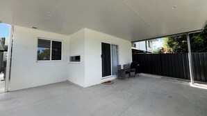 Un patio couvert avec une porte-fenêtre coulissante, une petite table avec des chaises et un barbecue noir.