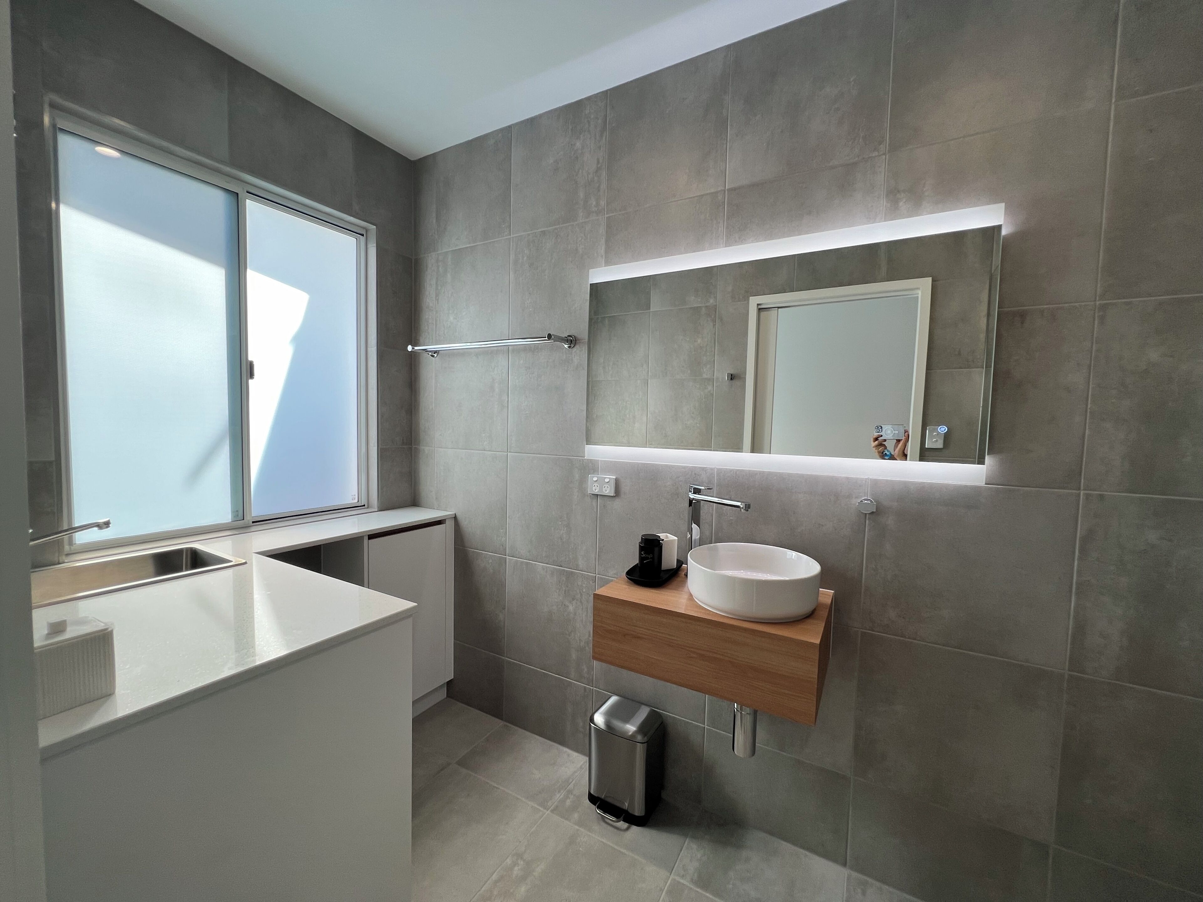 Un baño moderno con un ventanal grande, lavamanos empotrado, espejo y toallero.