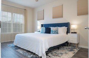 A modern bedroom with a large bed, a nightstand, and a window with sheer curtains.