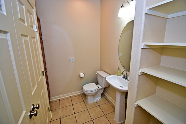 A bathroom with a toilet, sink, and shelves.