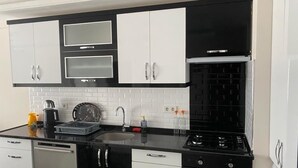 A modern kitchen with black and white cabinetry, a black countertop, a dishwasher, a stove, and a sink. - Fethiye Marinada lüks daire (Fethiye)
