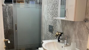 A modern bathroom with a glass shower enclosure, a toilet, and a sink with a mirror. - Fethiye Marinada lüks daire (Fethiye)