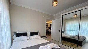 A hotel room with a large bed, a separate sleeping area, a bathroom with a mirror, and a dining area in the background. - Fethiye Marinada lüks daire (Fethiye)
