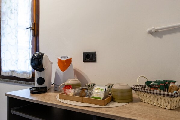 Una kitchenette con cafetera, hervidor de agua, una cesta de aperitivos y un refrigerador pequeño.