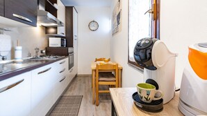 Een kleine keuken met witte kastjes, een houten stoel, een klok en een koffiezetapparaat.