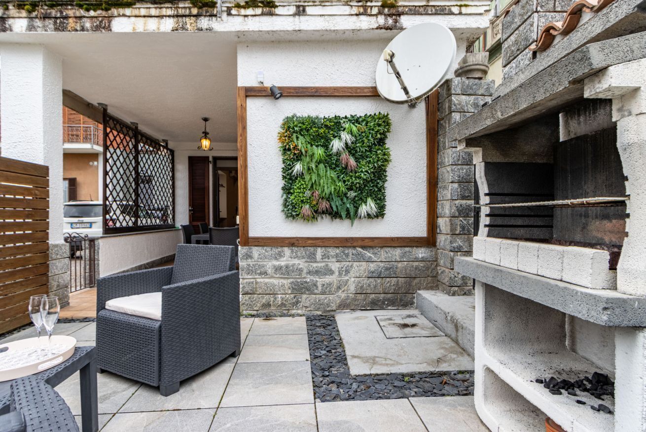Eine Terrasse im Freien mit Korbmöbeln, einer Wand mit Bepflanzung, einer Satellitenschüssel und einem Steinkamin.
