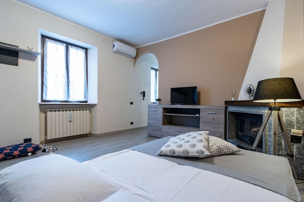 A bedroom with a bed, a TV, a fireplace, and a window.