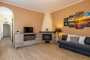 Ein Wohnzimmer mit Kamin, einer Couch, einem Fernseher und einem Bild an der Wand.