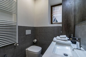 Un baño moderno con inodoro, lavabo, toallero y una ventana con una bandera.