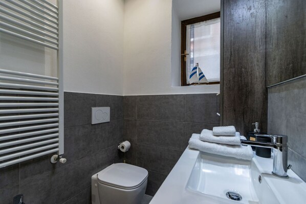 Une salle de bain moderne équipée de toilettes, d’un lavabo, d’un porte-serviettes et d’une fenêtre sur laquelle flotte un drapeau.