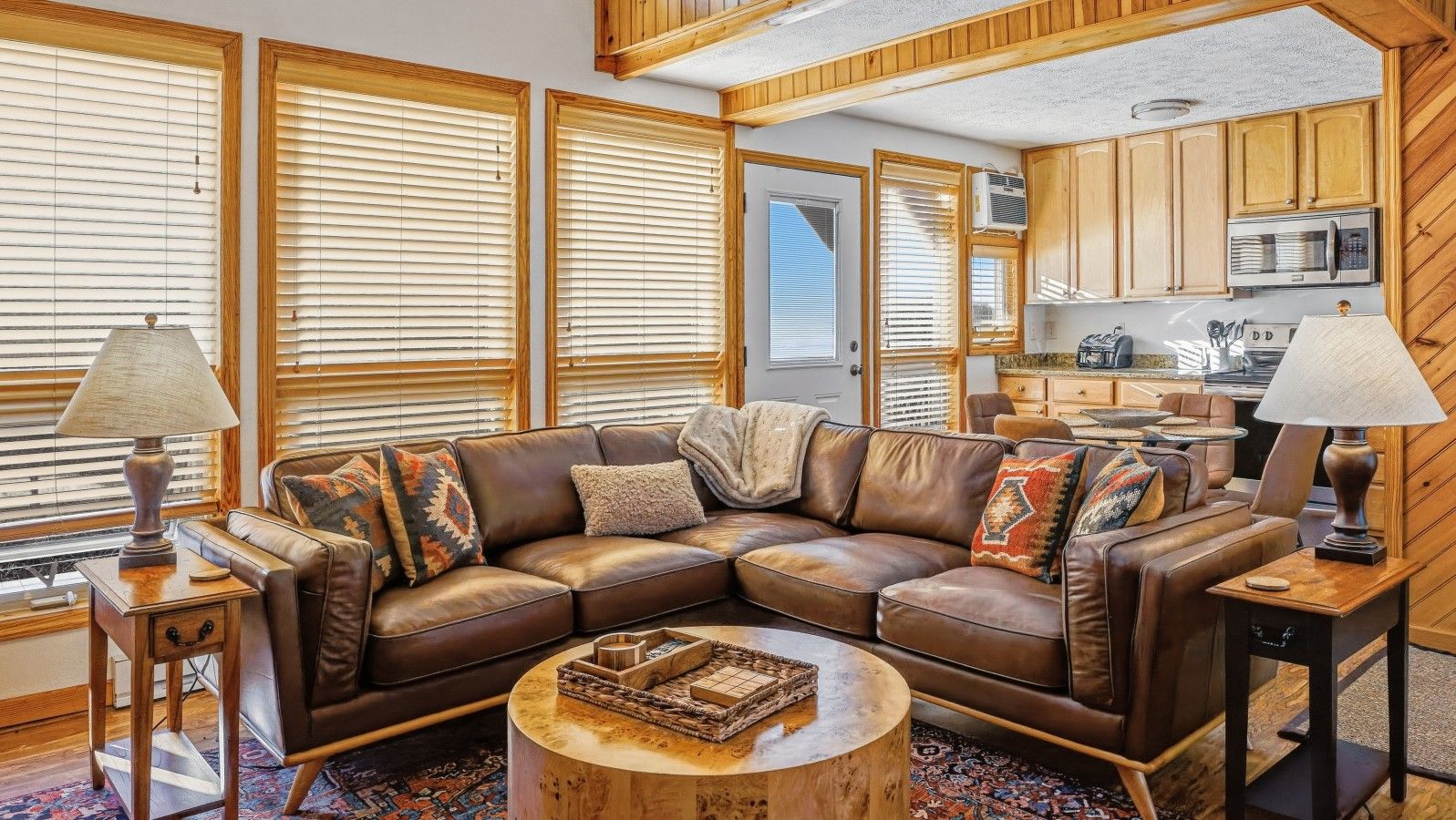 A cozy living room with a sectional sofa, a coffee table, and a kitchen area visible through an open door.