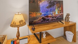 A television on a wooden stand with a remote control, a lamp with a nature-themed lampshade, and a small sculpture of a bear. - Fireplace, Deck, Walk to Slopes, Games, Views (Beech Mountain)