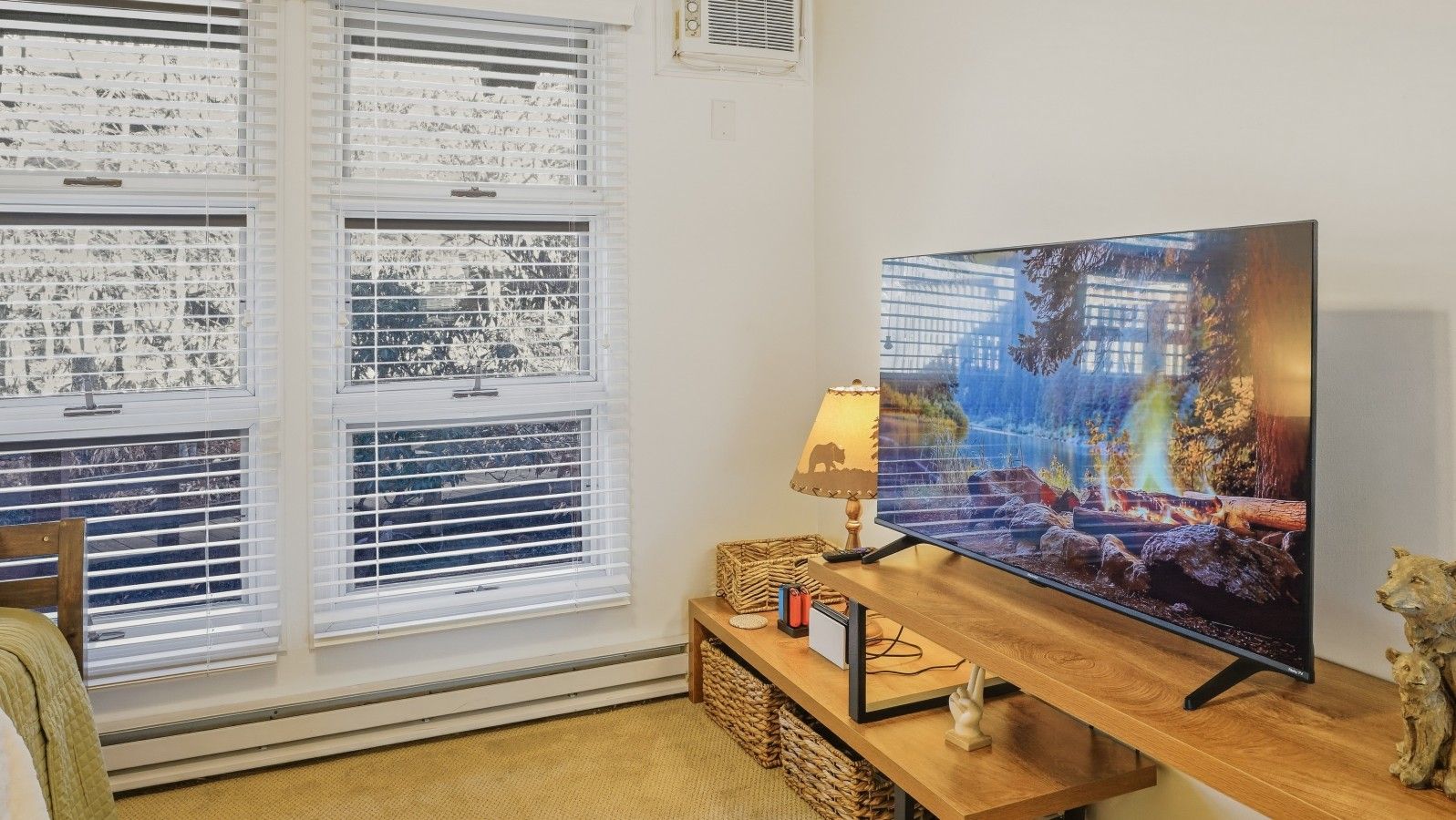 A living room with a large flat-screen TV on a wooden stand, a lamp, and a decorative animal figurine.