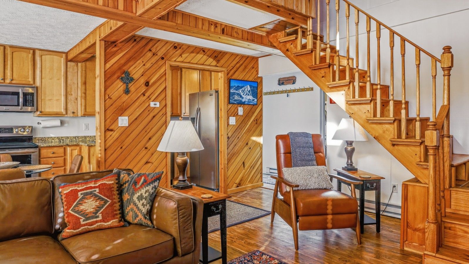 A cozy living room with a wooden staircase, a leather sofa, and a dining area.