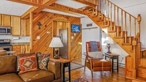 Una sala de estar acogedora con una escalera de madera, un sofá de cuero y un comedor.