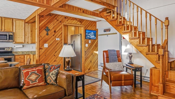 A cozy living room with a wooden staircase, a leather sofa, and a dining area.