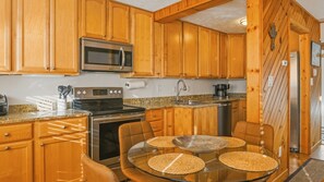 A kitchen with wooden cabinets, a stainless steel microwave, a stove, and a dining table with woven placemats. - Fireplace, Deck, Walk to Slopes, Games, Views (Beech Mountain)
