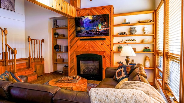 Ein gemütliches Wohnzimmer mit Kamin, Holzregalen, einem Fernseher und einer Treppe.