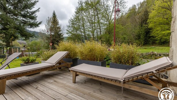 A wooden deck with four lounge chairs, surrounded by greenery and a stone wall. - House La Couze - CHAMBON SUR LAC (CHAMBON SUR LAC)