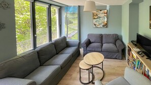 A modern living room with a grey sofa, a small round table, a bookshelf, and a TV. - House La Couze - CHAMBON SUR LAC (CHAMBON SUR LAC)