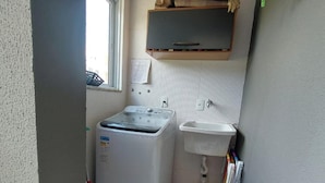 Een kleine wasserette met een wasmachine, een wasbak en een raam.