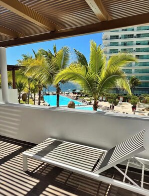 A poolside area with lounge chairs, palm trees, and a view of a building with multiple floors. - The One & Only Luxe Beachfront Villa ~ Hotel Zone (Puerto Vallarta)