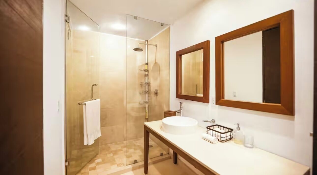 Un baño con cabina de ducha de vidrio, un lavabo con espejo y una mesa de madera.