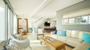 A spacious living area with a sofa, chairs, a coffee table, a TV, and a staircase leading to an upper level. - The One & Only Luxe Beachfront Villa ~ Hotel Zone (Puerto Vallarta)