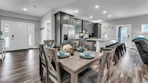 Une cuisine moderne avec des meubles de couleur sombre, un îlot central et un coin repas comprenant une table et des chaises en bois.