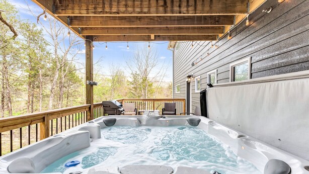 Un bain à remous sur une terrasse en bois, avec vue sur les arbres et un bâtiment.
